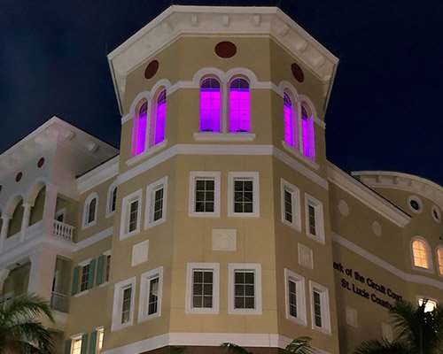 St. Lucie County Clerk's building at night with windows lighting up in purple